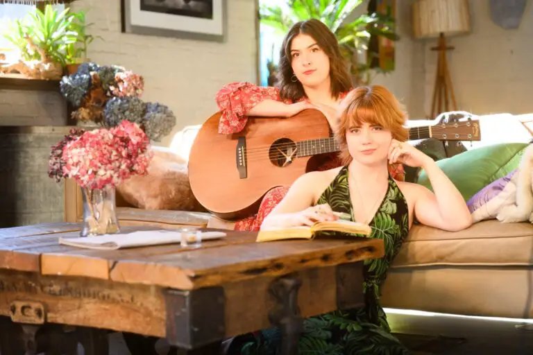 portrait of Maria Isabella Andreoli with a guitar on a couch and EmmaLee Kidwell on the floor with an open notebook surrounded by flowers.