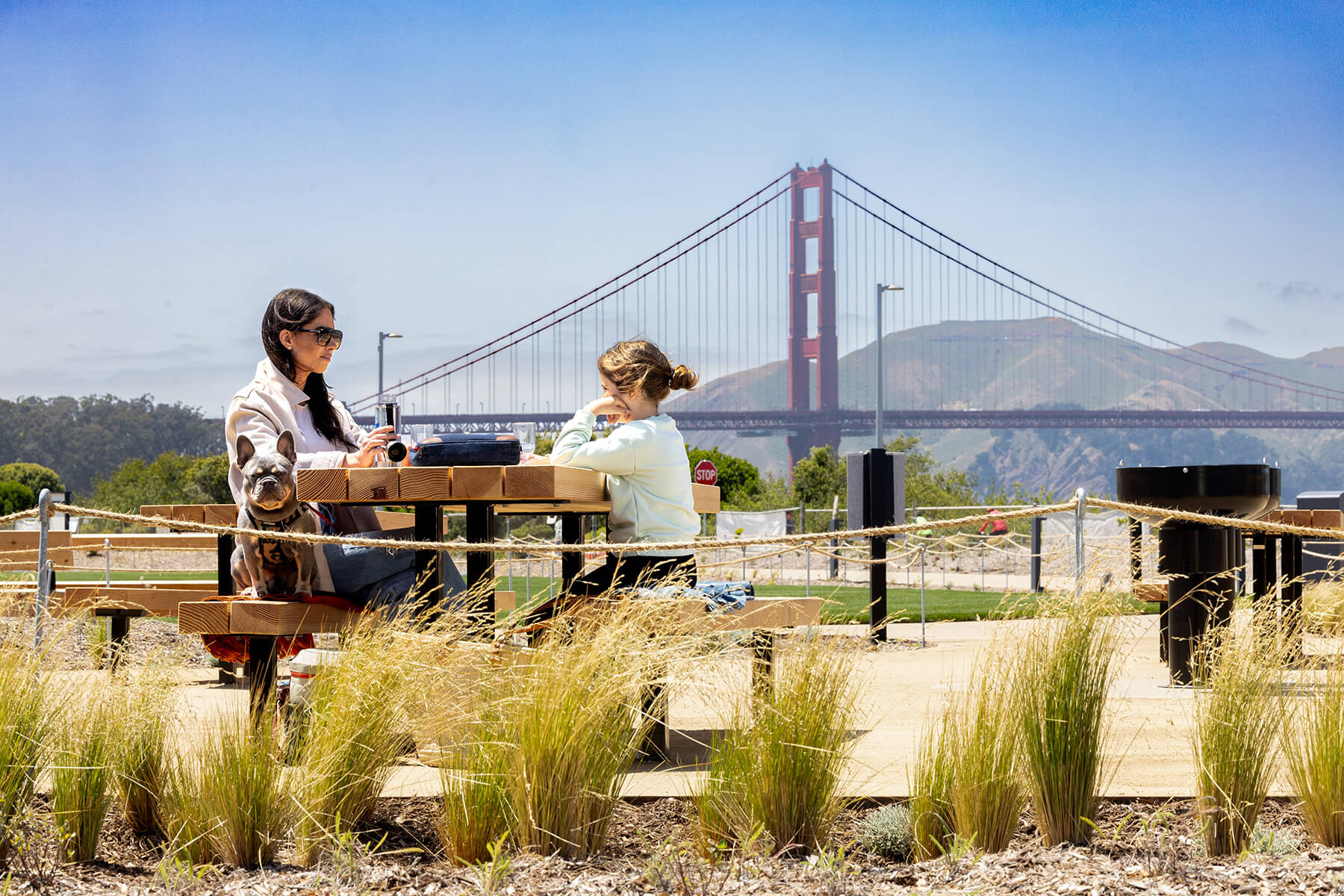 A woman and child sit at a picnic table in Presidio with the Golden Gate Bridge behind them
