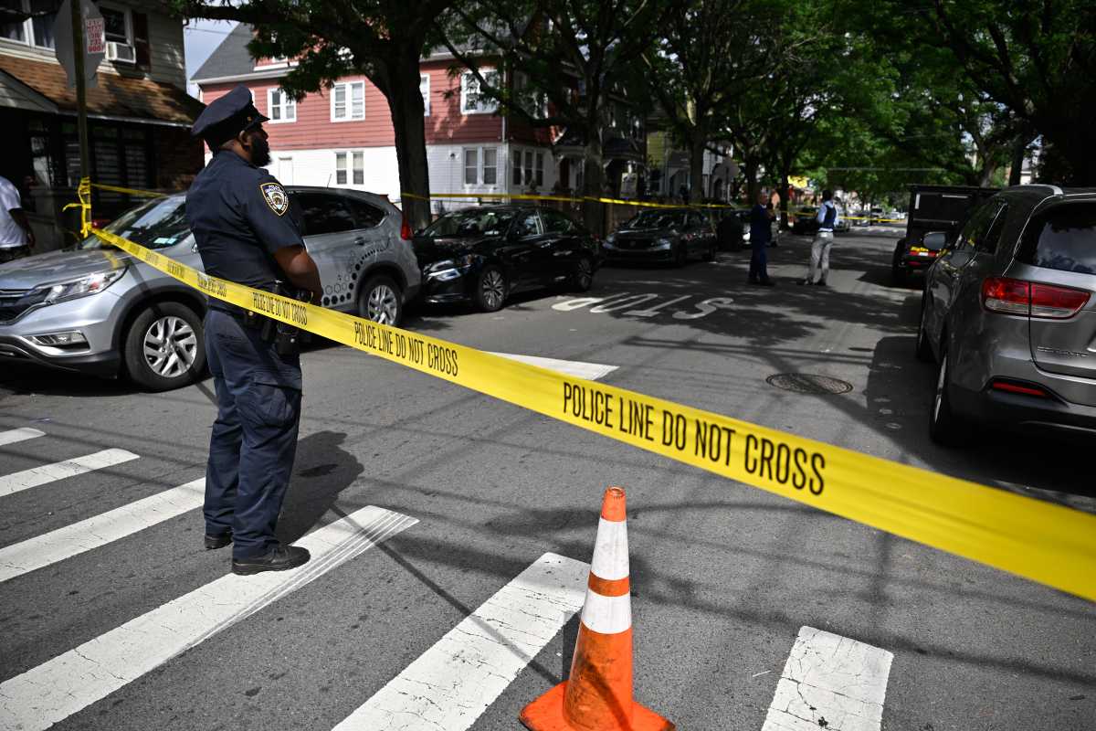 Queens man shot dead on residential block; cops seek suspect 2 officer standing at shooting scene on street with yellow crime scene tape stretched