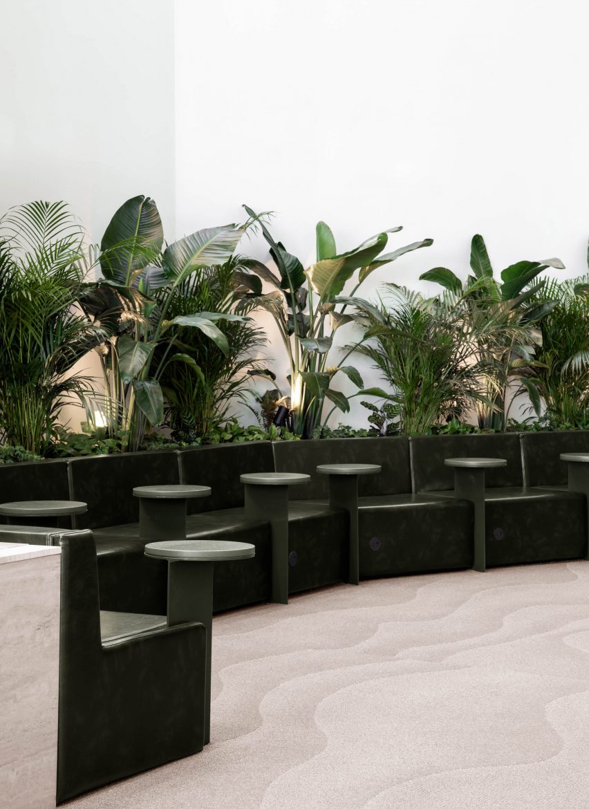 Line of green seats with individual tables, and plants behind