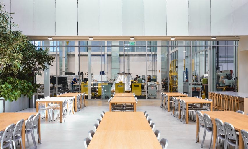 Photo of the long tables in the all-hands area of the Vast headquarters, with a glass wall beyond that showing the clean-room fabrication zone