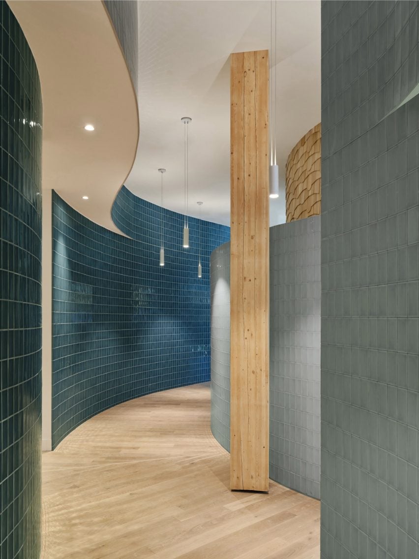 Curved corridor lined with blue tiles and featuring recessed doorways