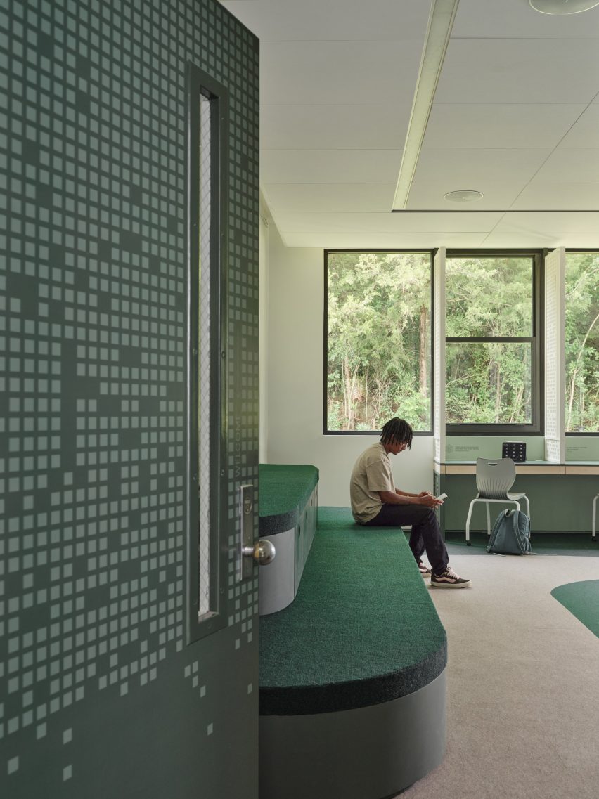 View through an open door into a classroom, where a boy is sat on a green bleacher seat