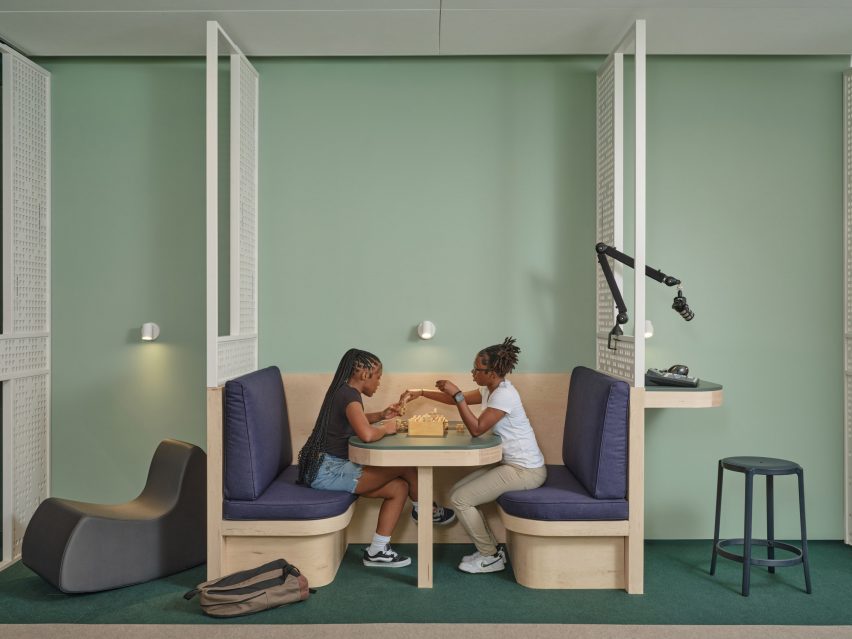 Two girls sat in a banquette in front of a pale green wall
