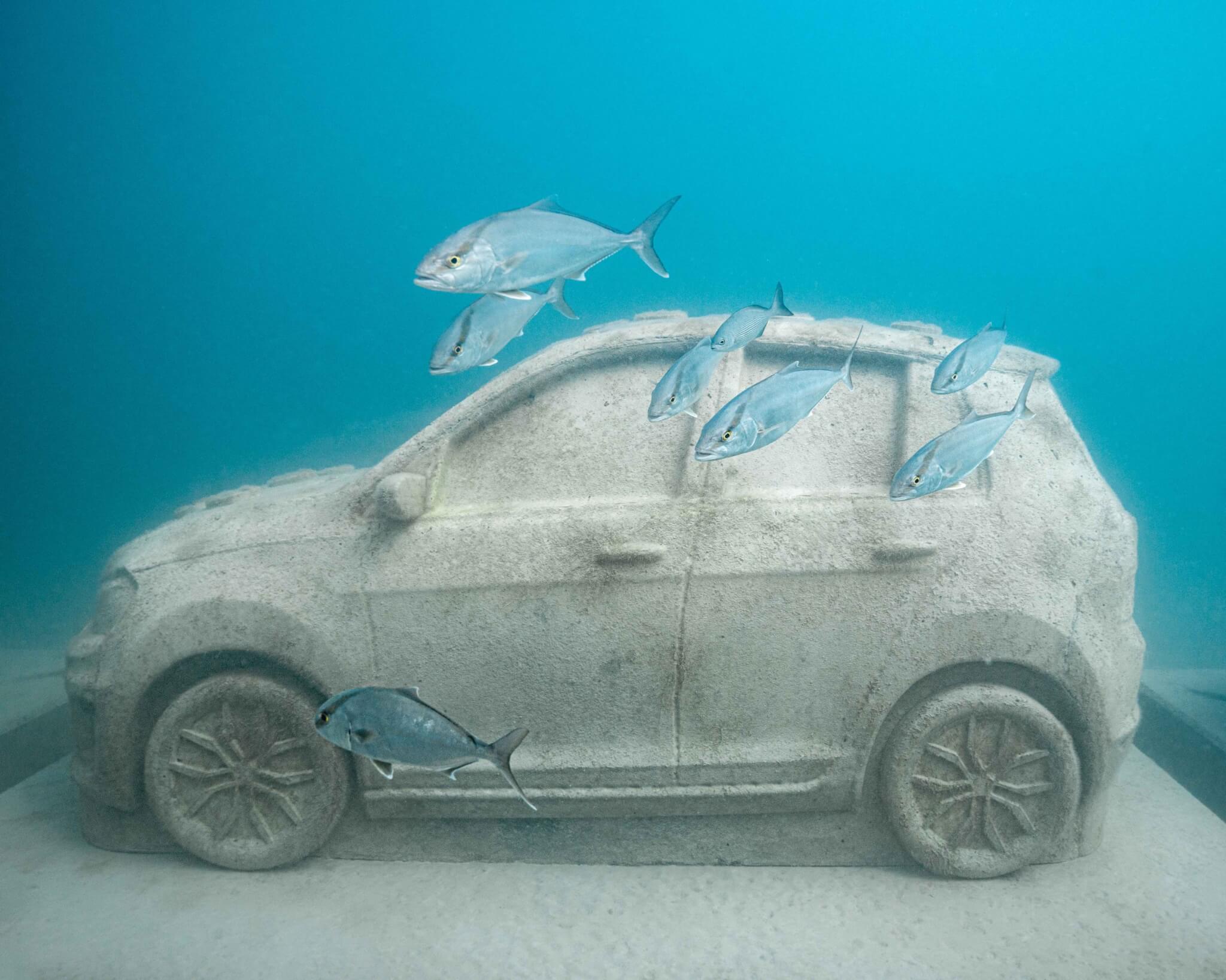 Close-up of concrete car statue with fish swimming past it