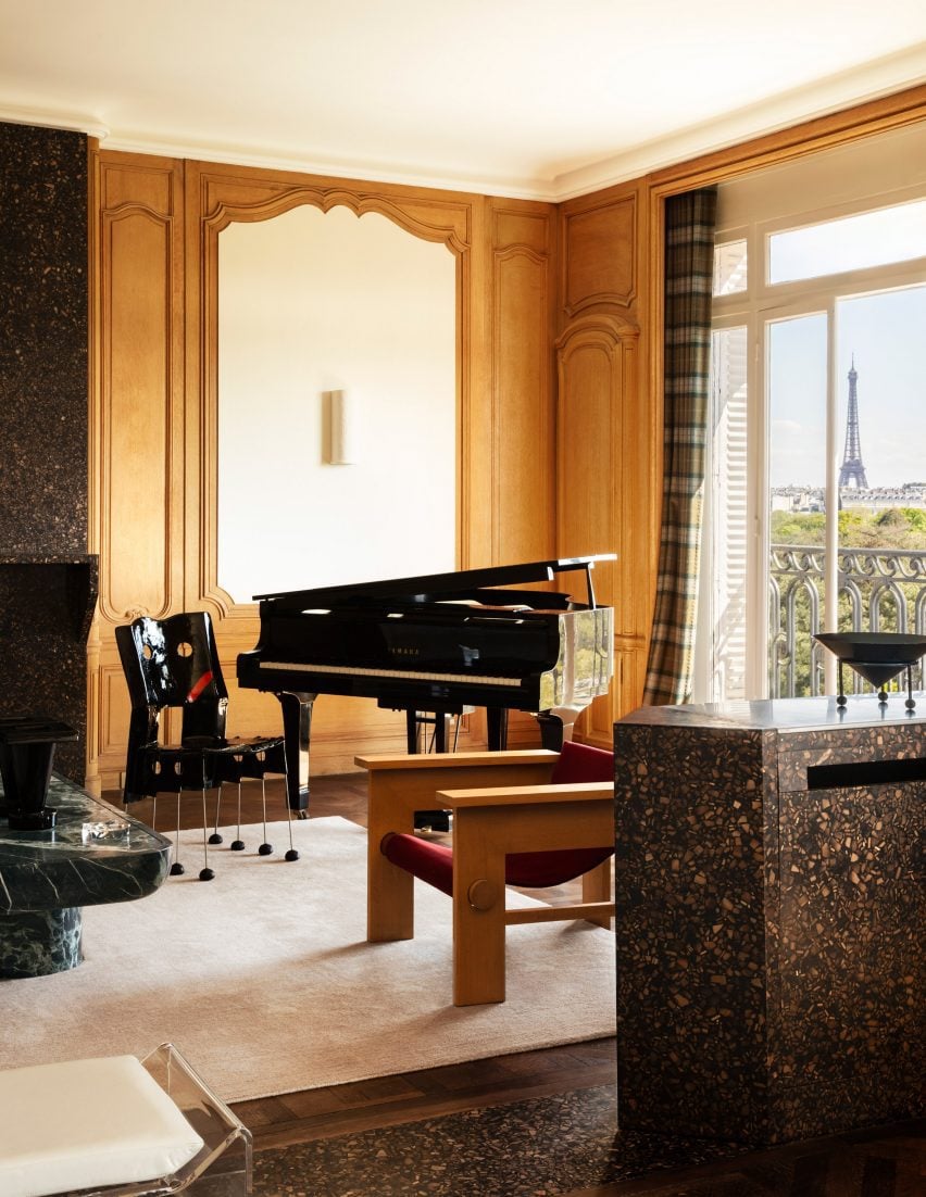 Photograph of a section of the double-living room, featuring a grand piano and a large window offering views of the Eiffel Tower