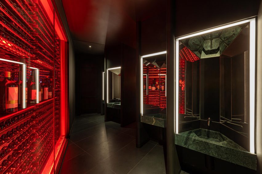 A glowing red wine rack forms a partition for a restaurant bathroom, which features green marble basins