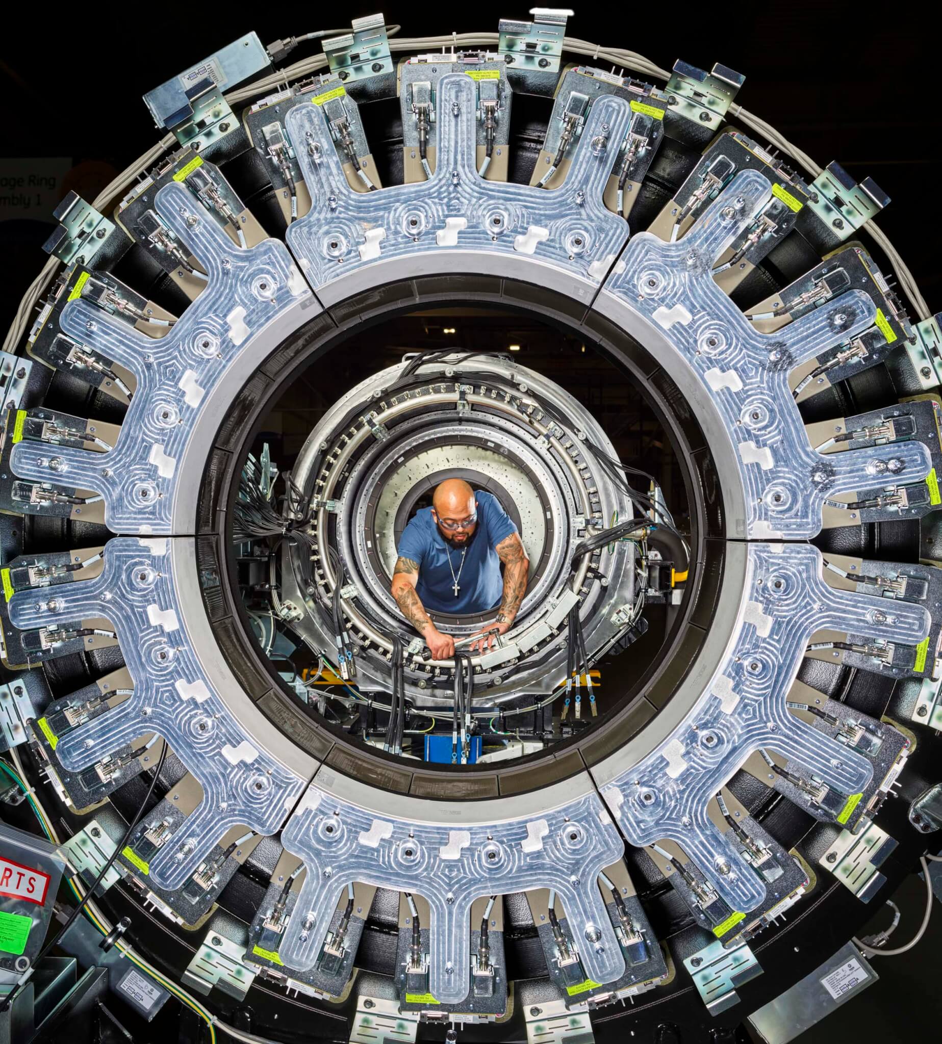 A technician works inside the circular bore of a PET scanner, framing him like a mechanical iris.