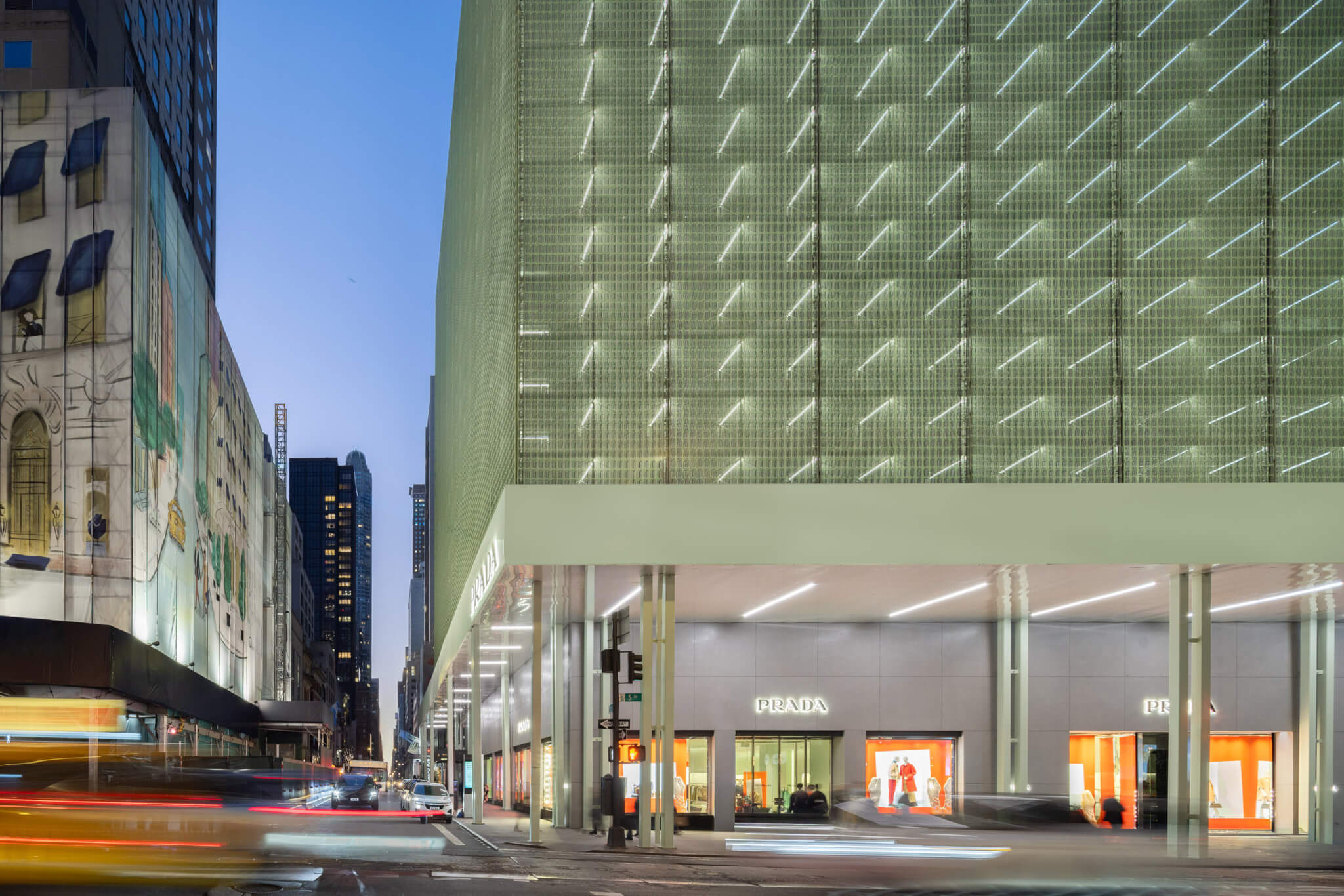 street level of scaffolding and scrim fabrics on facade of prada building lit up at night